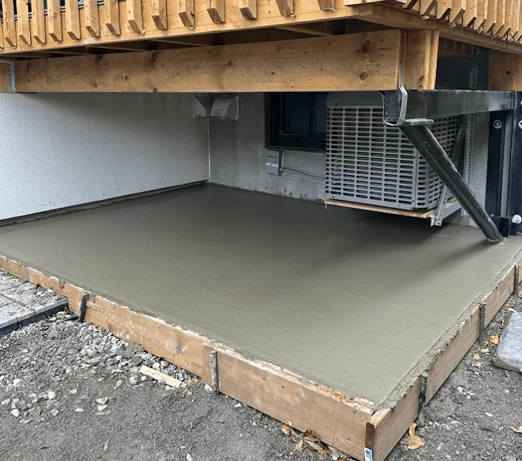 Freshly poured residential concrete pad beneath a home's deck