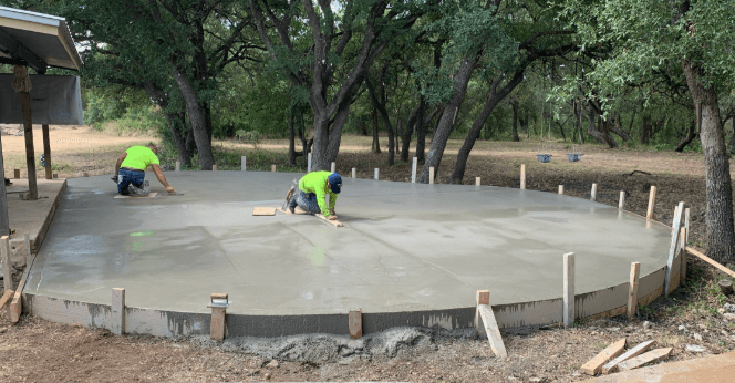 Crew finishing a newly poured round concrete patio surrounded by trees
