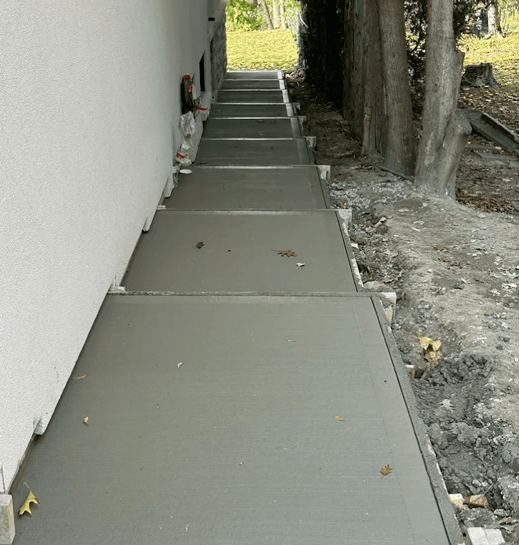 Concrete walkway installation running alongside a home's foundation